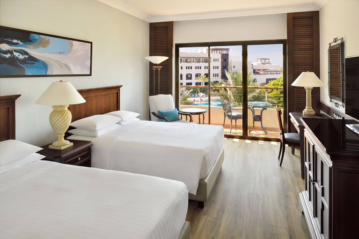 A hotel room with two beds, a balcony with a pool, and a TV.