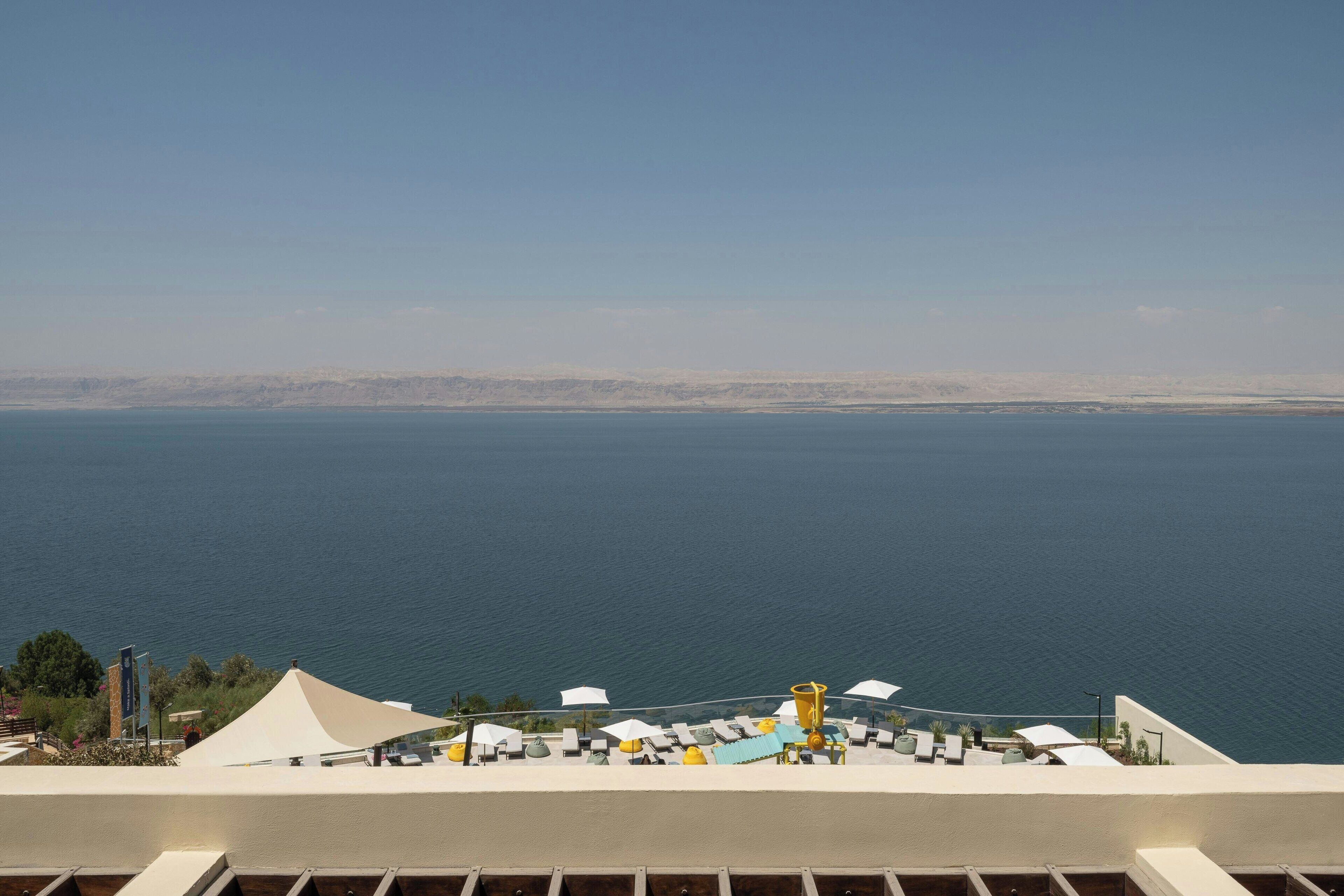 Blick auf das Meer mit einer Terrasse, ausgestattet mit Liegestühlen und Sonnenschirmen.