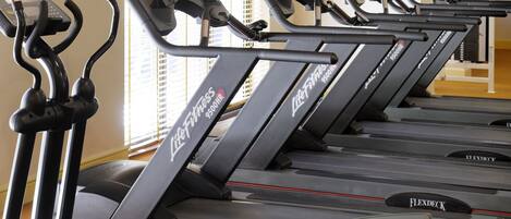 A row of treadmills in a gym with a TV mounted on the wall.