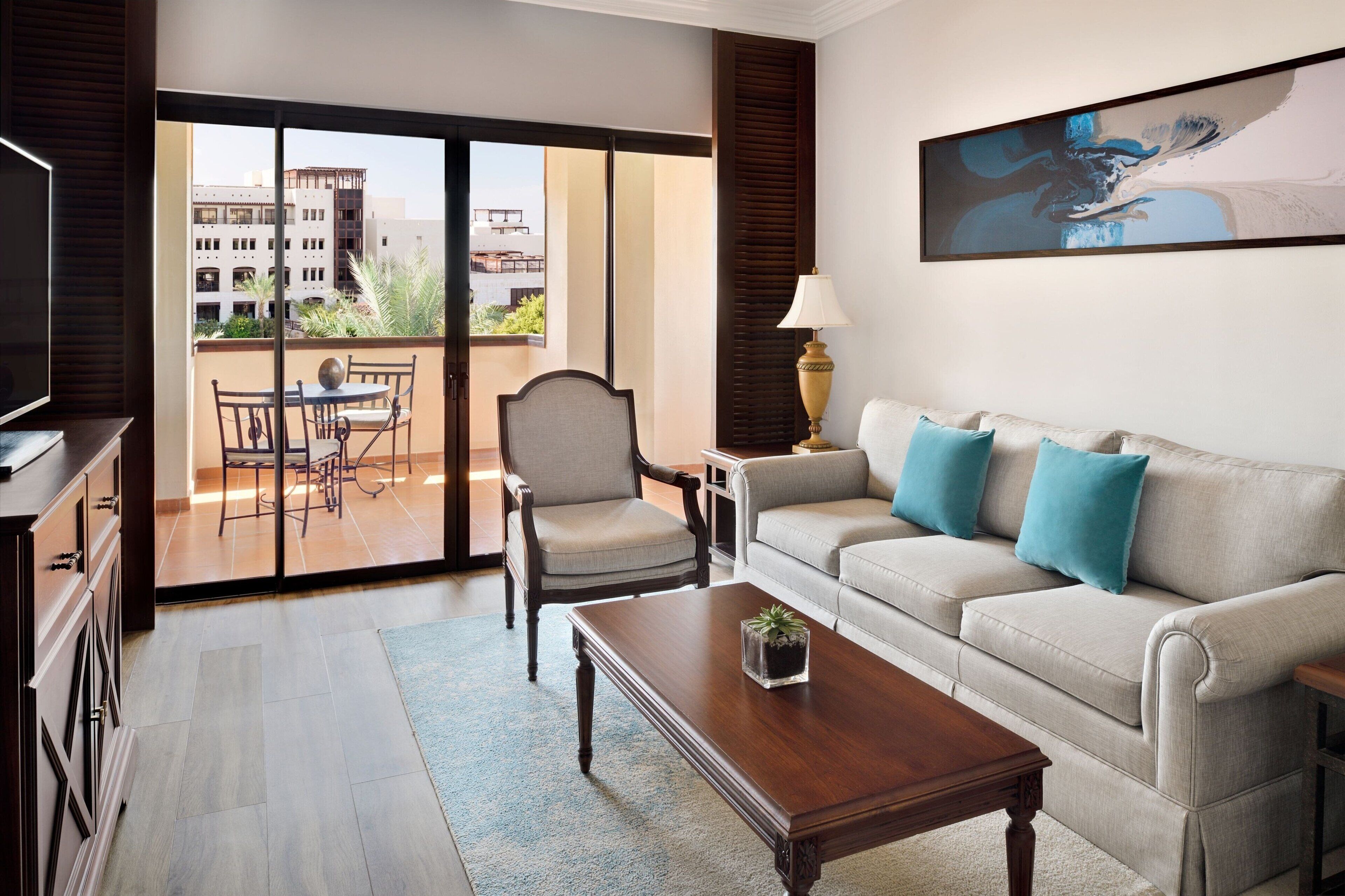 Sala de estar com sofá, poltrona, mesa de centro e televisão. Varanda com mesa e cadeiras.