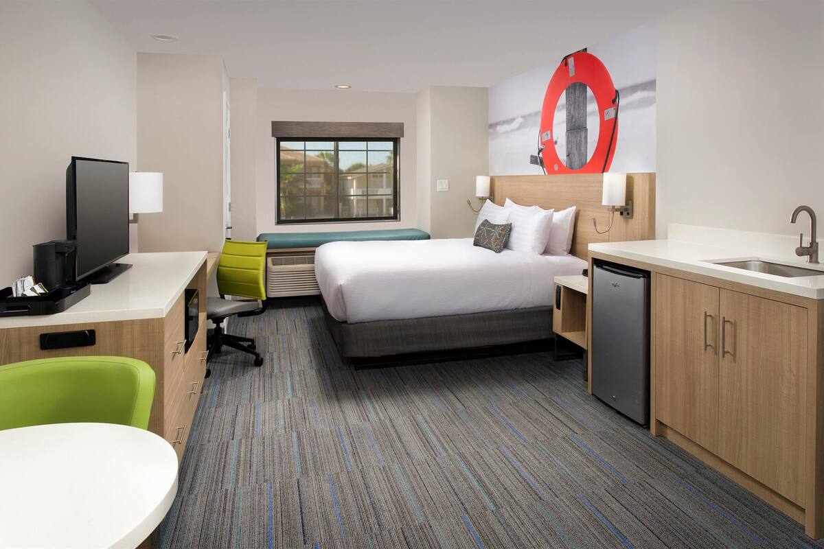 A hotel room with a bed, desk, chair, and a window with a view.