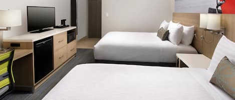 A hotel room with two beds, a desk with a television, a microwave, and a small seating area.