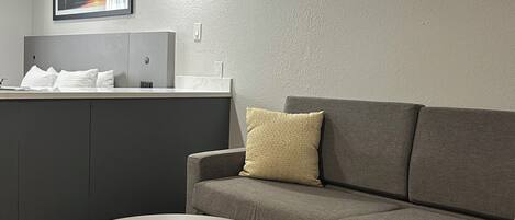 A modern hotel room with a grey sofa, a yellow side table, and a framed picture on the wall.