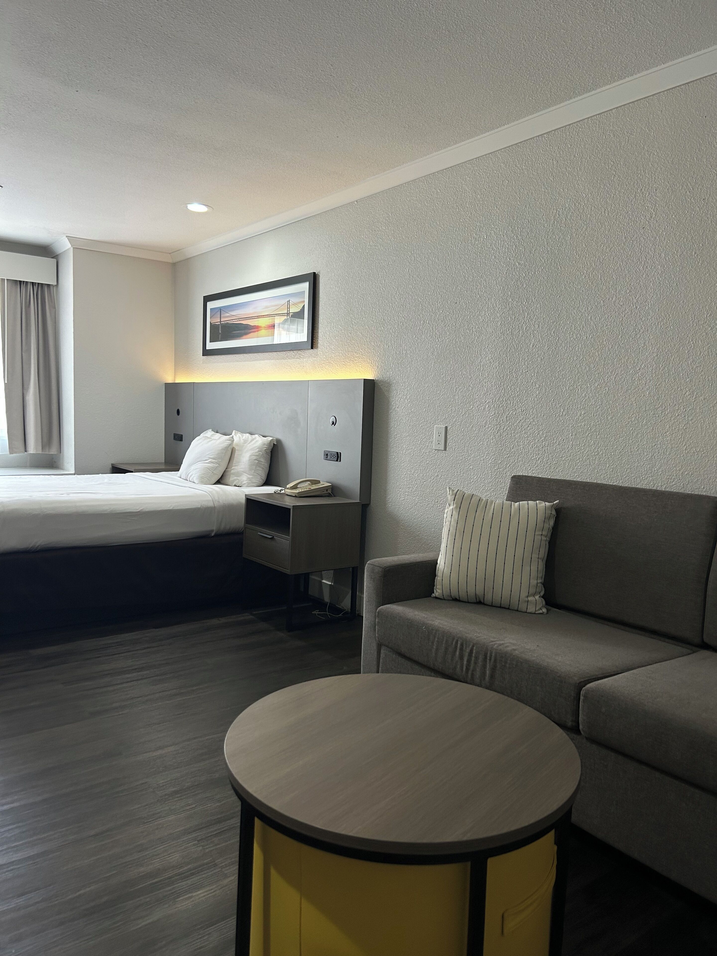 A hotel room with a bed, a bedside table with a phone, a sofa, and a small round table.
