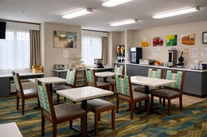A hotel dining area with multiple tables and chairs, a coffee machine, and a refrigerator.