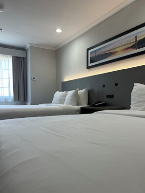 A hotel room with two beds, a headboard with a mounted phone, and a painting above the headboard.