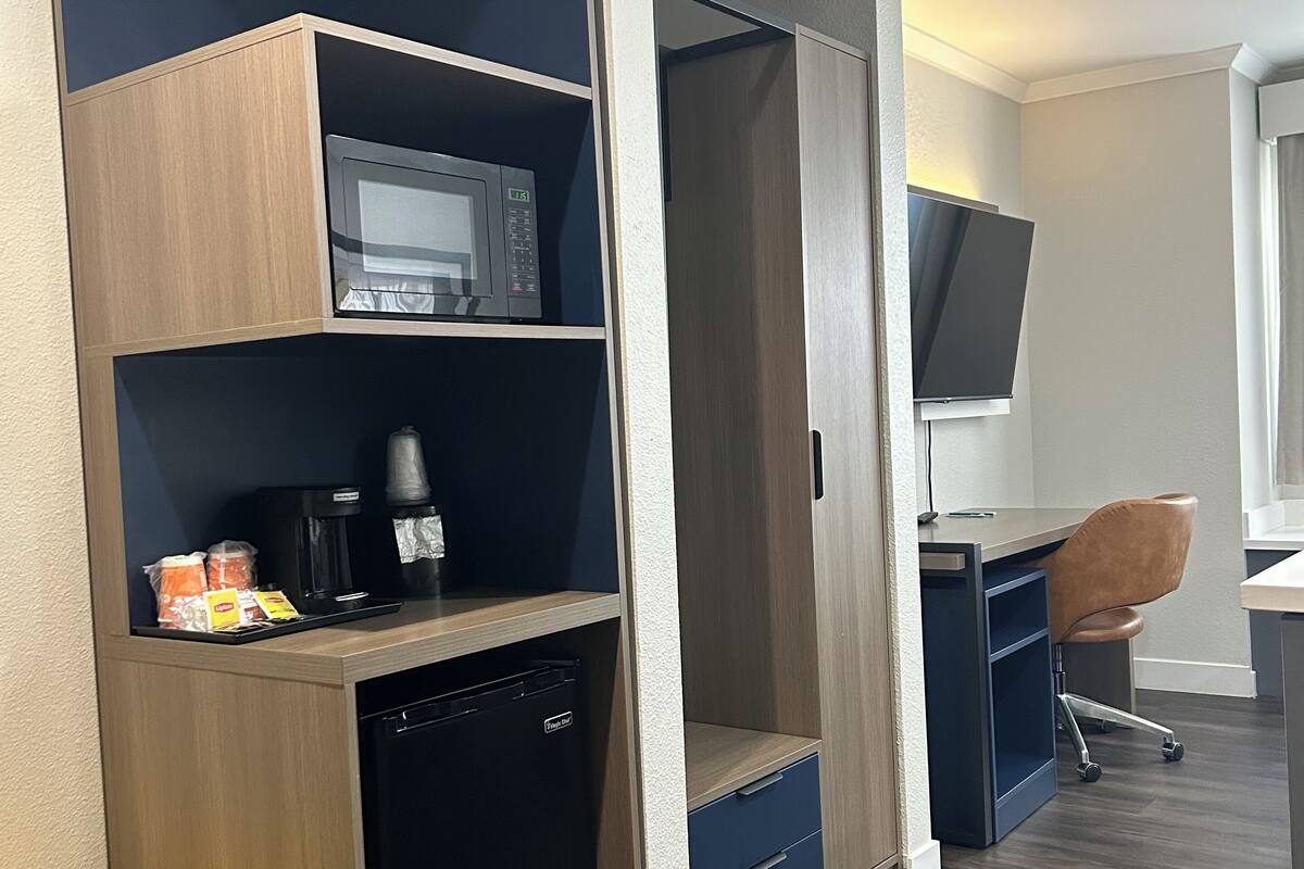 A compact hotel room with a kitchenette, a microwave, a coffee maker, and a TV.