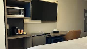 A hotel room with a bed, a desk with a microwave, a refrigerator, a flat-screen TV, and a coffee maker.