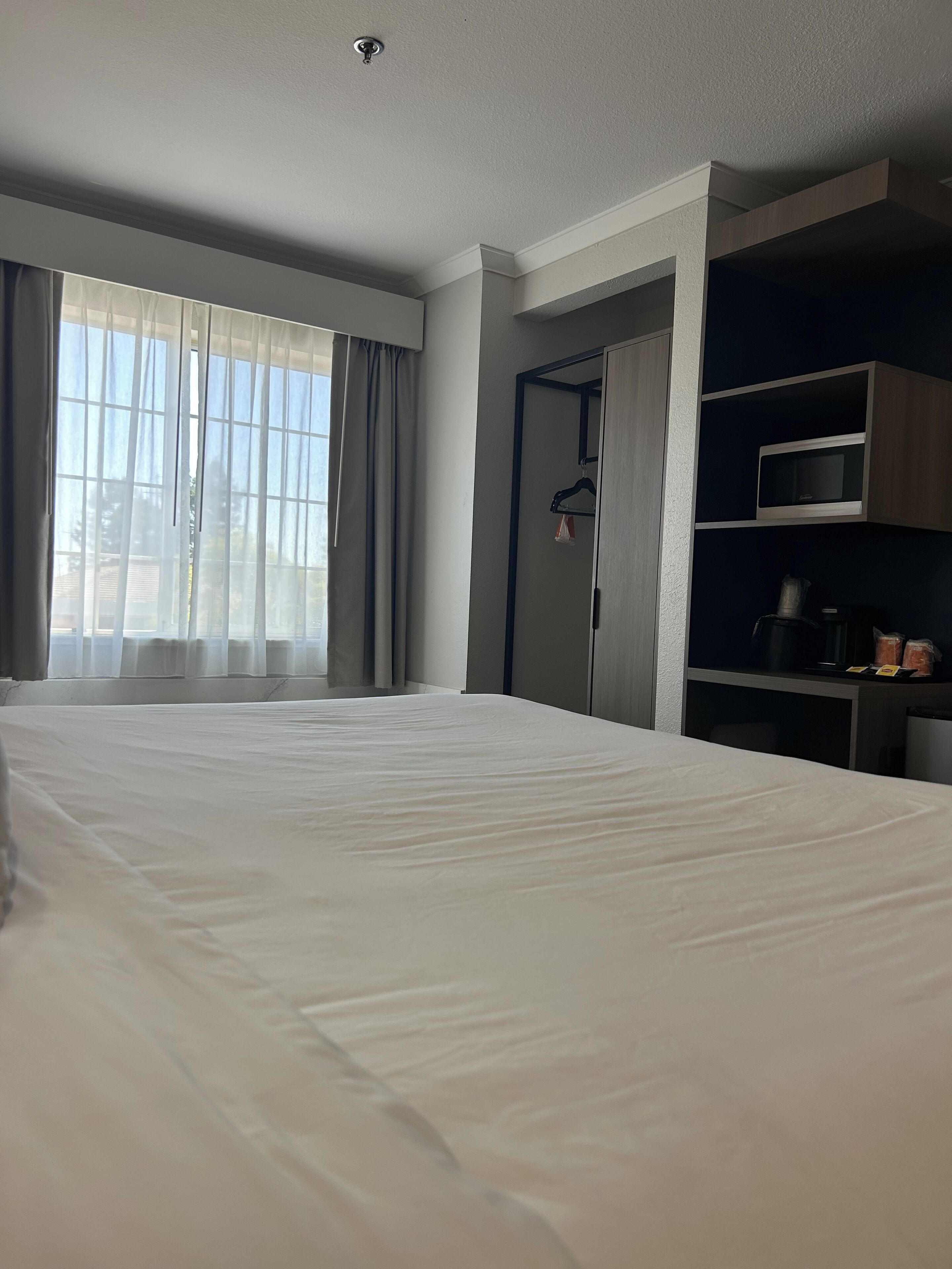 A hotel room with a large bed, a wardrobe, a microwave, and a small kitchen area.