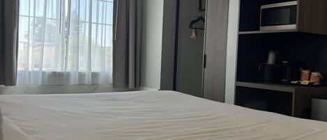 A hotel room with a large bed, a wardrobe, a microwave, and a small kitchen area.
