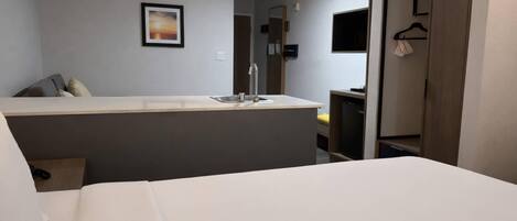 A hotel room with a bed, a small desk with a sink, a wardrobe, and a framed picture on the wall.