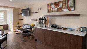 A modern hotel lobby with a wooden reception desk, a comfortable seating area with a sofa and chairs, a flat-screen TV mounted on the wall, and a decorative wall piece above the desk. - Econo Lodge Inn & Suites Santa Rosa South (Santa Rosa)