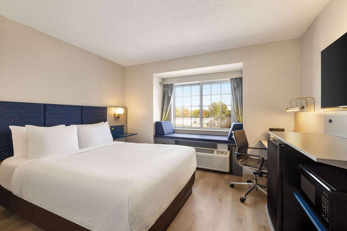 A hotel room with a large bed, a desk with a chair, a flat-screen TV, and a window with curtains.