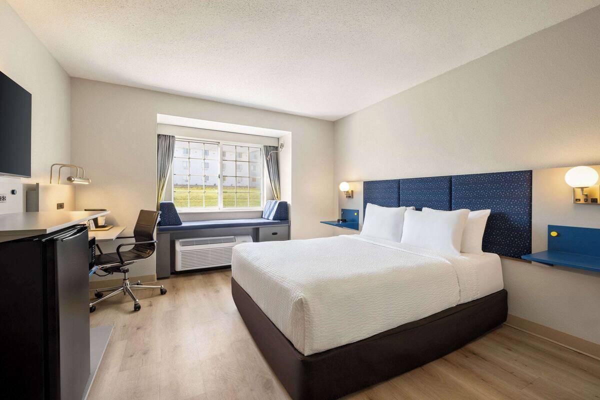 A hotel room with a bed, desk, chair, and a window with curtains.