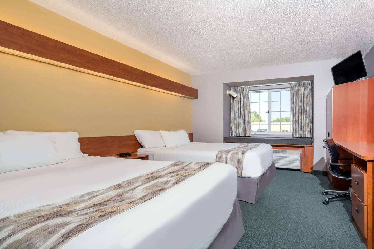 A hotel room with two beds, a desk, a television, and a window with curtains.