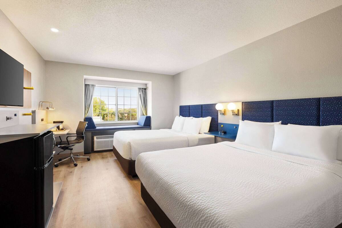 A hotel room with two beds, a desk with a chair, a TV, and a window with curtains.