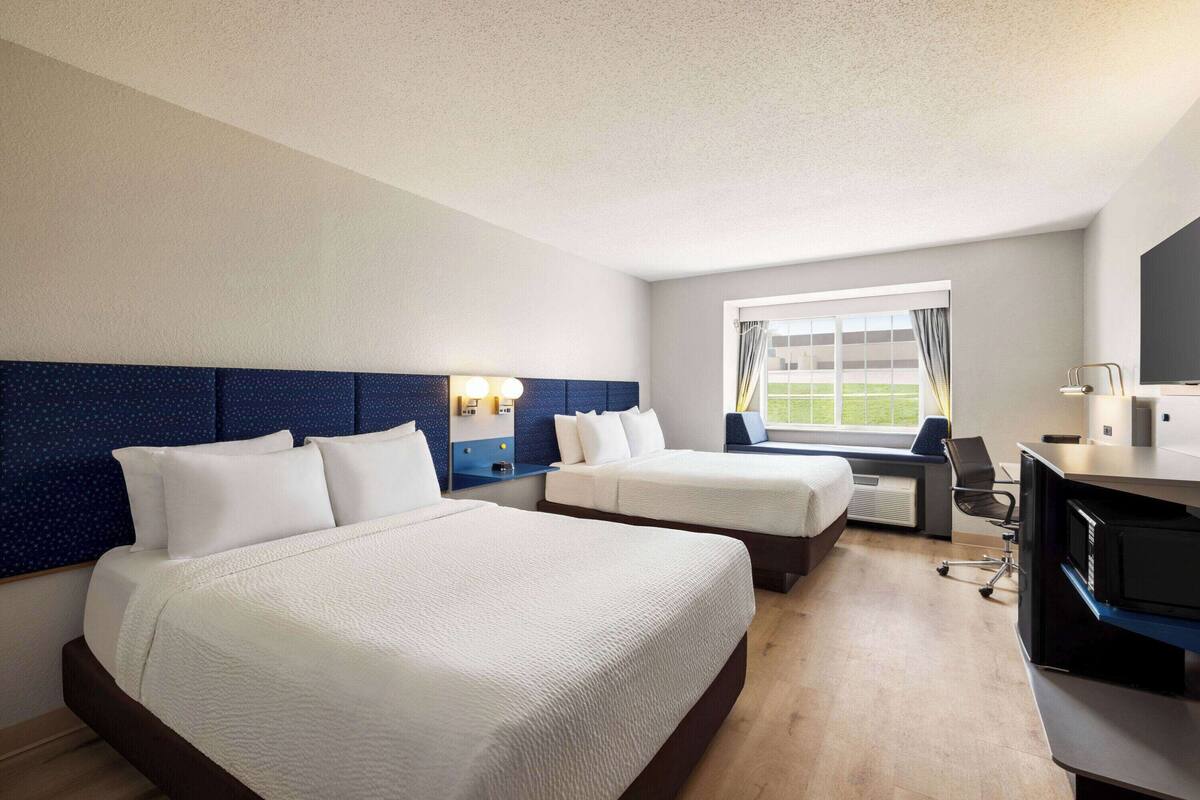A hotel room with two beds, a desk, and a large window.