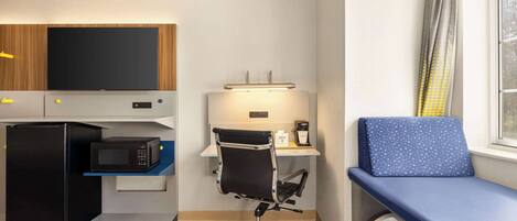 Habitación de hotel compacta con kitchenette, escritorio con silla, cama y ventana con cortinas.
