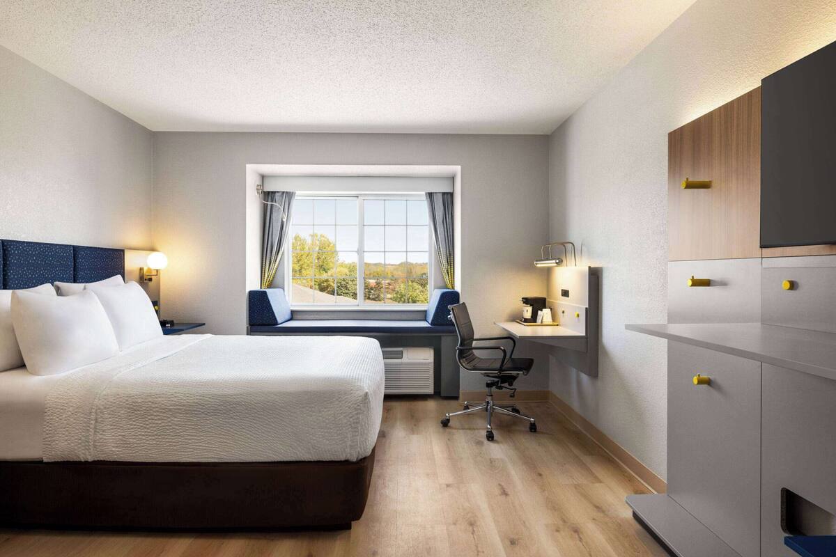 A modern hotel room with a large bed, a desk, and a view of the outdoors.