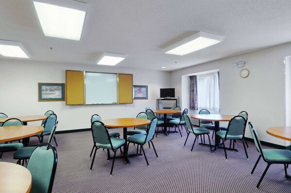 A conference room with multiple tables and chairs, a projector screen, a television, and a clock on the wall. - Microtel Inn & Suites by Wyndham New Ulm (New Ulm)