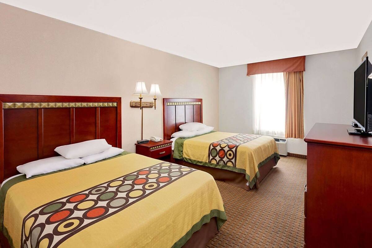 Ein Hotelzimmer mit zwei Betten, einem Schreibtisch, einem Fernseher und einem Fenster mit Vorhängen.