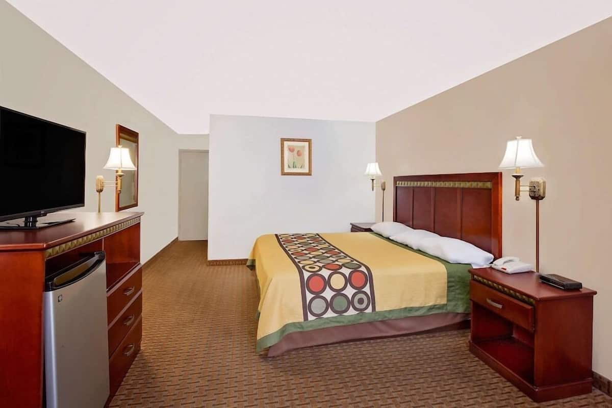 Ein Hotelzimmer mit Bett, Fernseher, Schreibtisch mit Lampe und kleinem Kühlschrank.