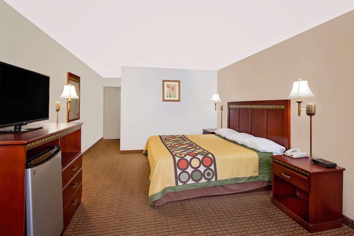 Ein Hotelzimmer mit einem Bett, einem Fernseher, einem Schreibtisch mit Lampe und einem kleinen Kühlschrank.
