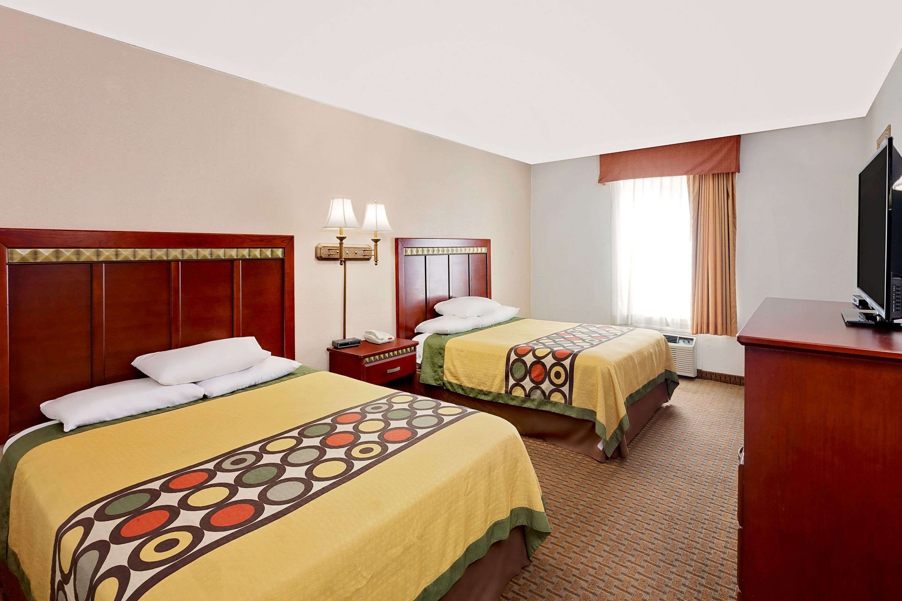 A hotel room with two beds, a desk, a TV, and a window with curtains.