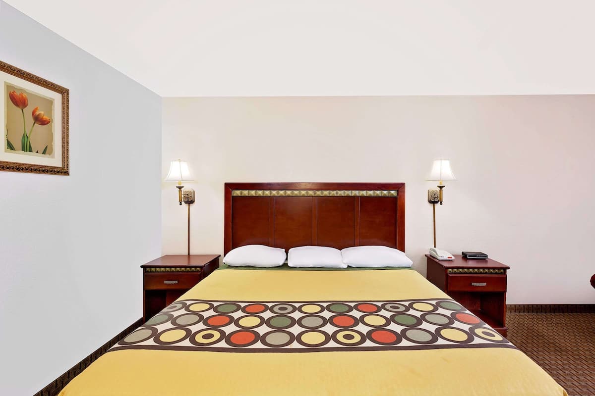 Ein Hotelzimmer mit einem großen Bett, zwei Nachttischen, einem Holzkopfteil und einer Wandlampe.