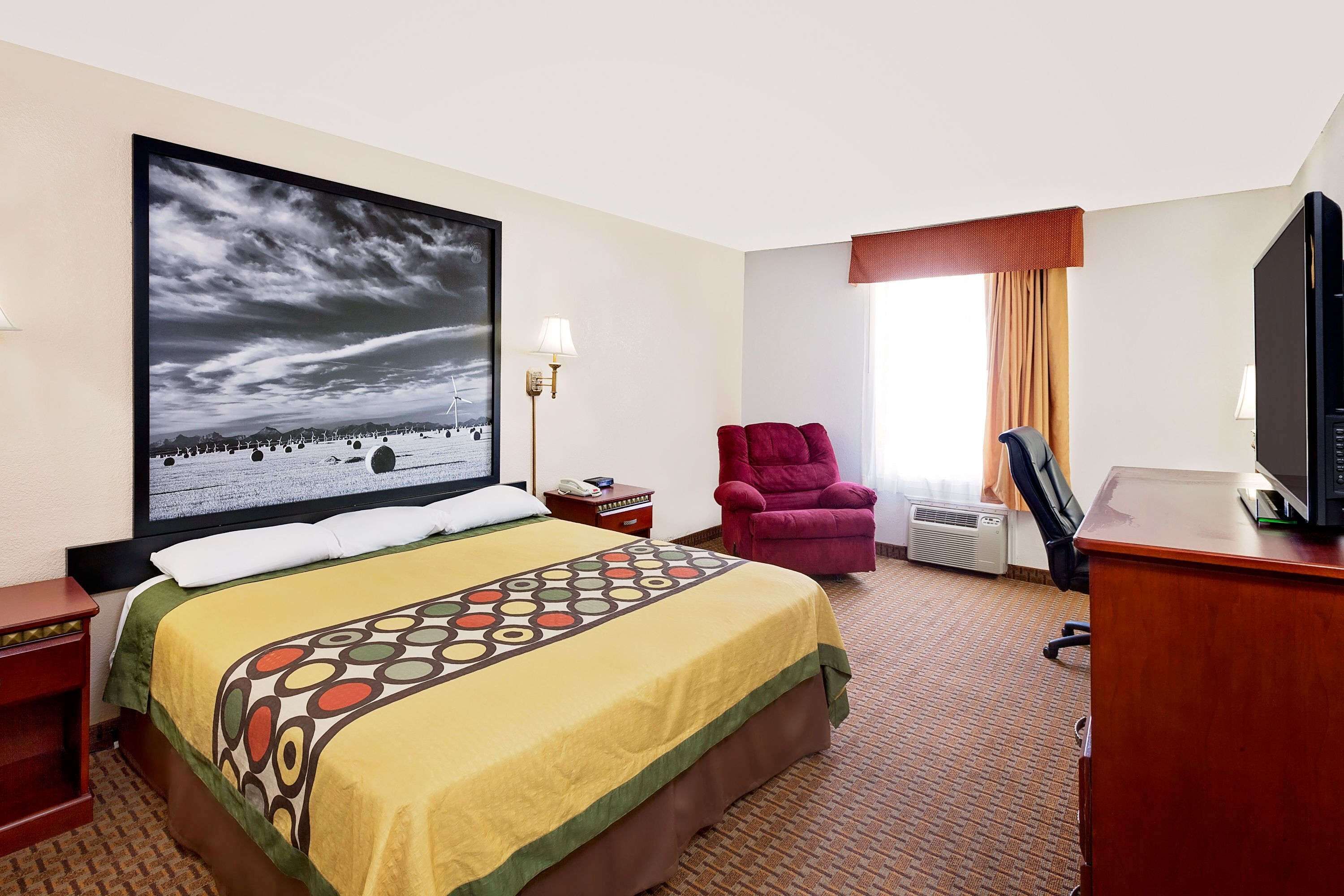 Een hotelkamer met een bed, een bureau, een stoel, een televisie en een groot schilderij aan de muur.