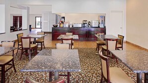 Eine Hotelhalle mit mehreren Esszimmertischen und Stühlen, einem Empfangsbereich und einem gemusterten Teppich.