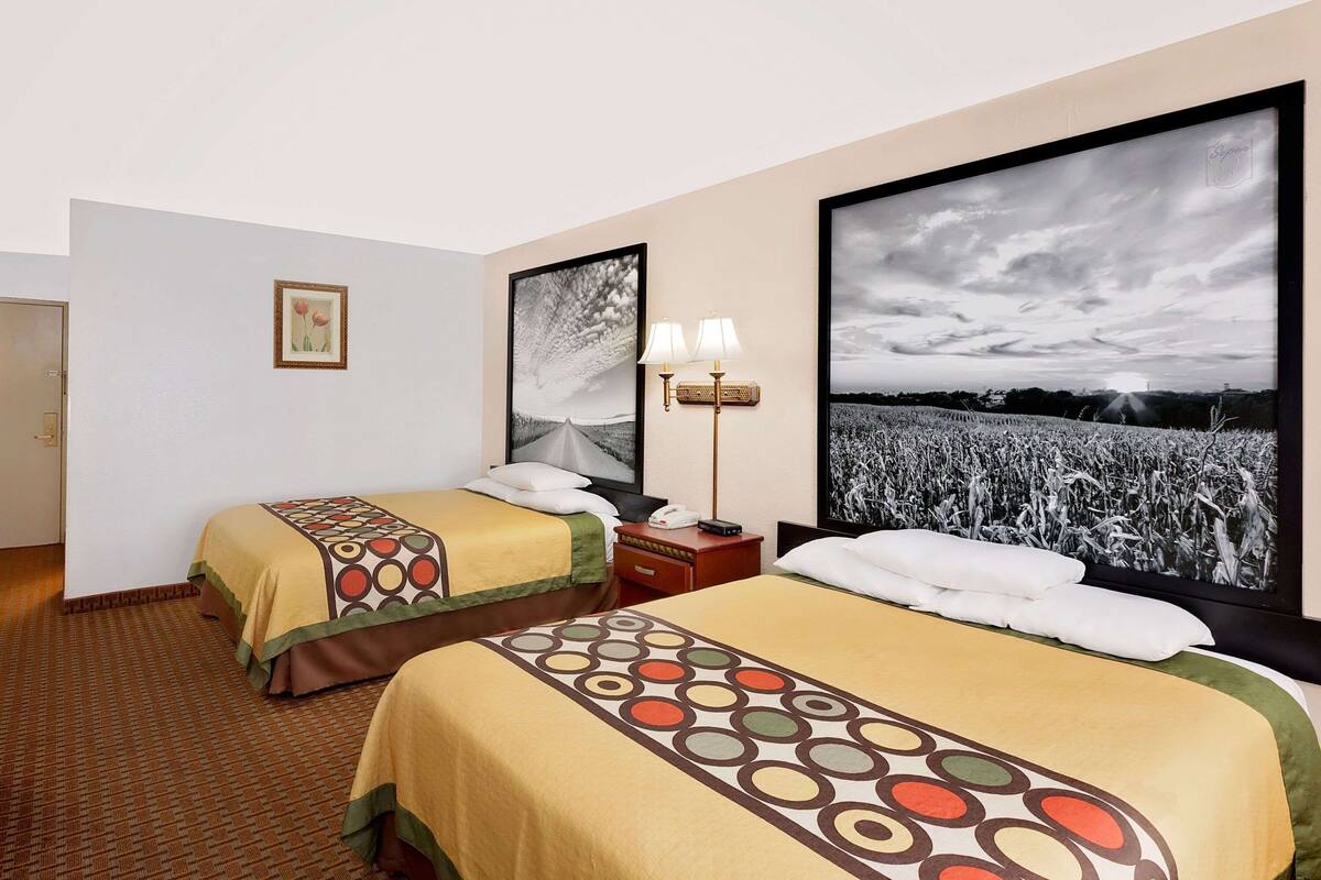 Ein Hotelzimmer mit zwei Betten, einem Nachttisch, einer Lampe und großen gerahmten Bildern an der Wand.