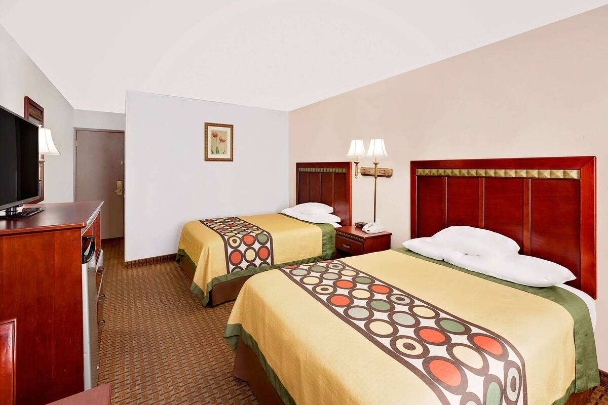 Ein Hotelzimmer mit zwei Betten, einem Fernseher, einem Schreibtisch und einer Lampe.