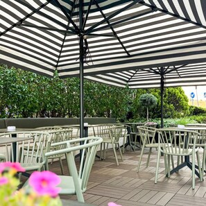 Outdoor seating with striped umbrellas, surrounded by greenery.