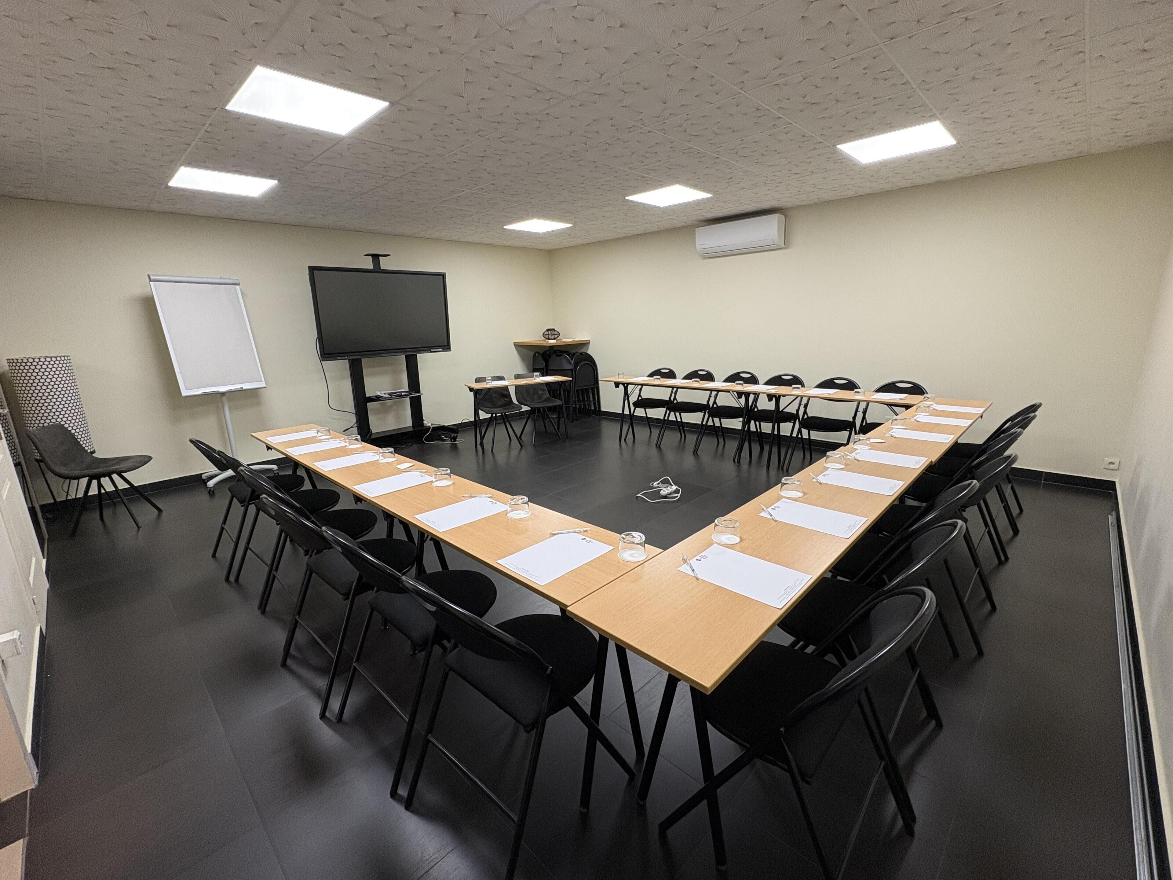A conference room with a long table, black chairs, a whiteboard, a projector screen, and an air conditioning unit.