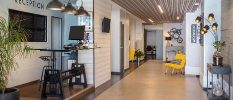 A reception area with a modern design, featuring a reception desk, a seating area with a yellow chair, and a staircase leading to another floor.