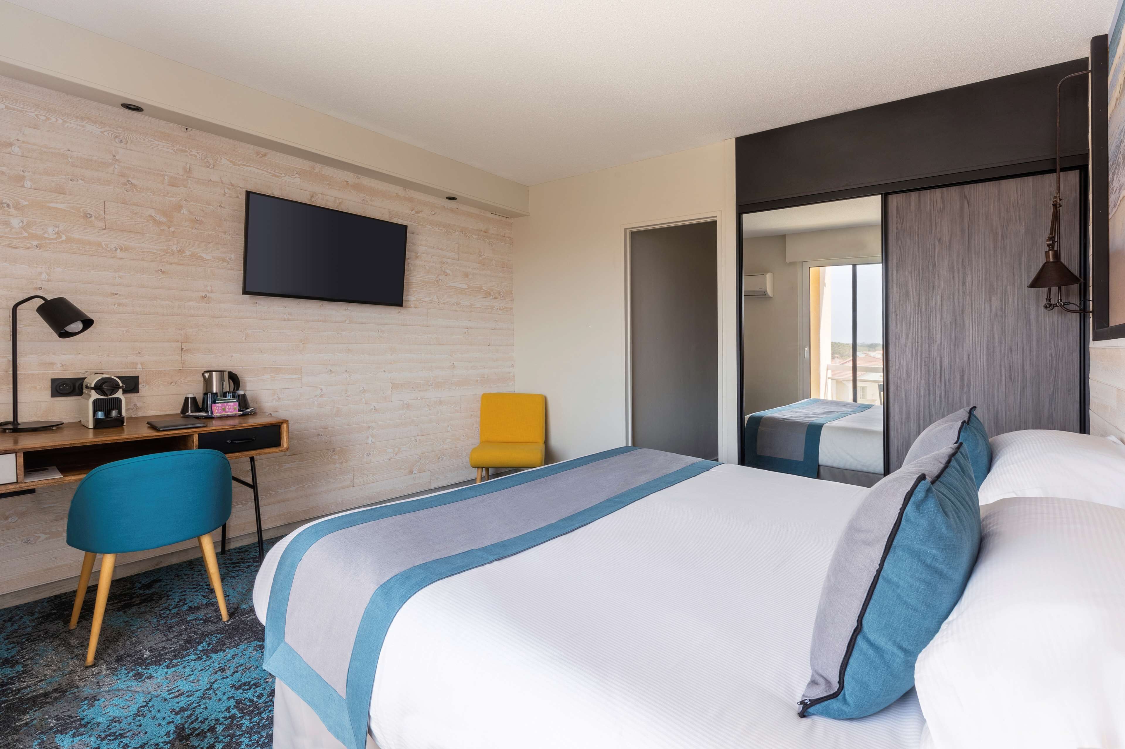A hotel room with a bed, a desk with a chair, a television, and a mirror.