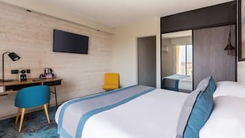 A hotel room with a bed, a desk with a chair, a television, and a mirror.