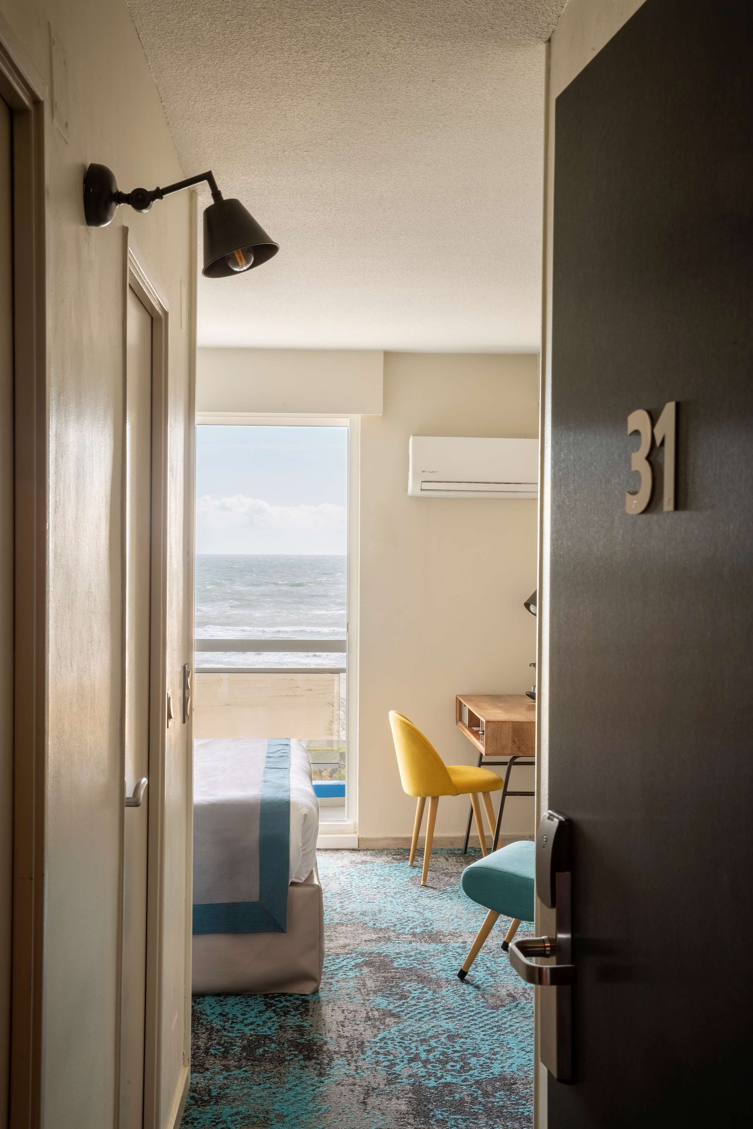 A hotel room with a bed, a desk, a chair, and a view of the ocean.