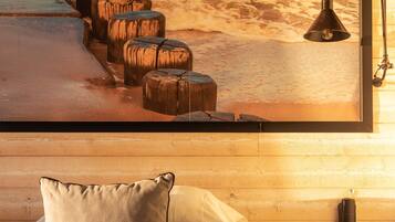 A hotel room with a bed, pillows, a bedside table with a cup, and a wall-mounted lamp.