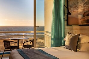Une chambre d’hôtel avec un lit, une table, deux chaises, une vue sur l’océan et un rideau.