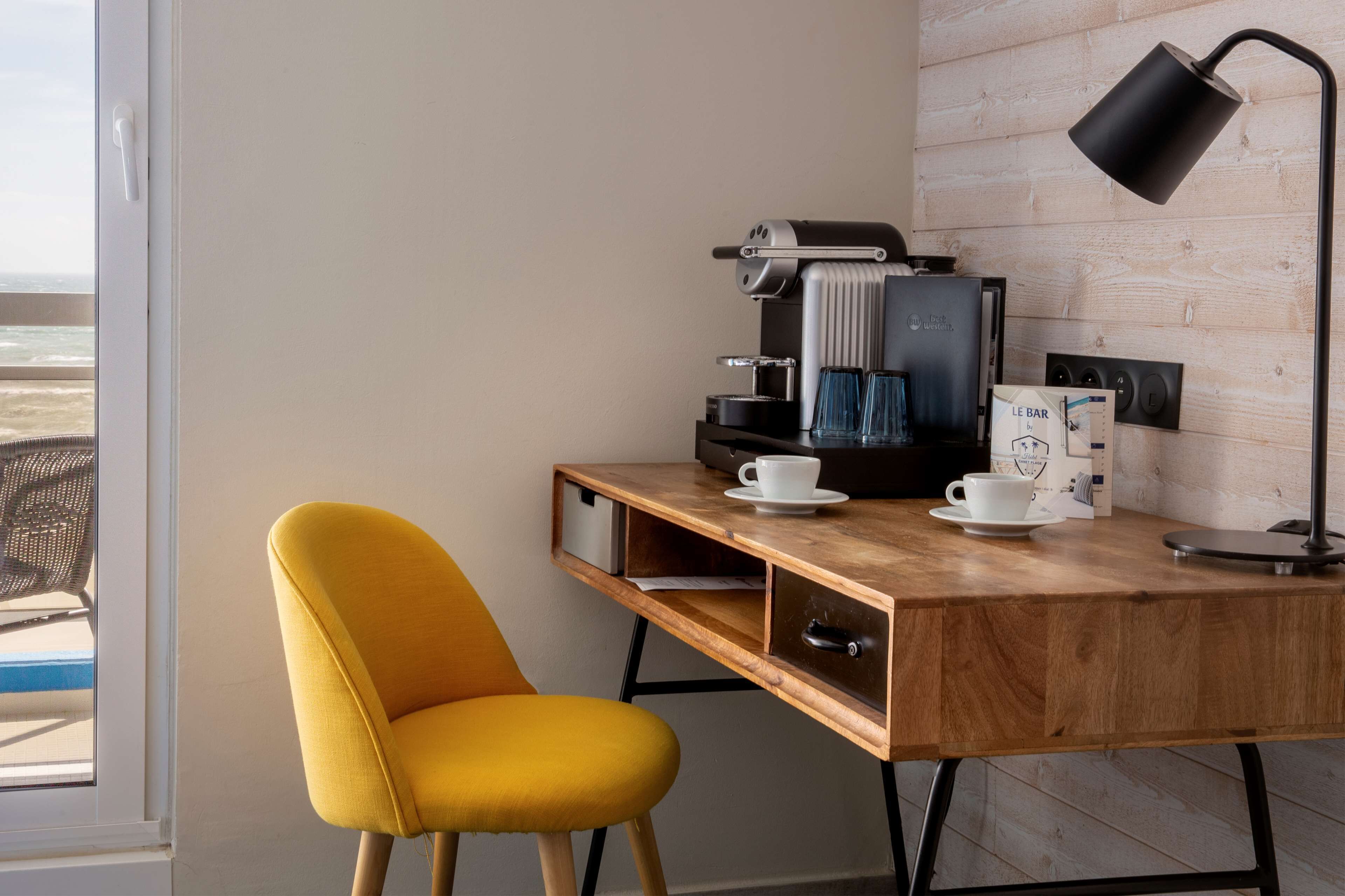 A wooden desk with a coffee machine, a cup, and a lamp.