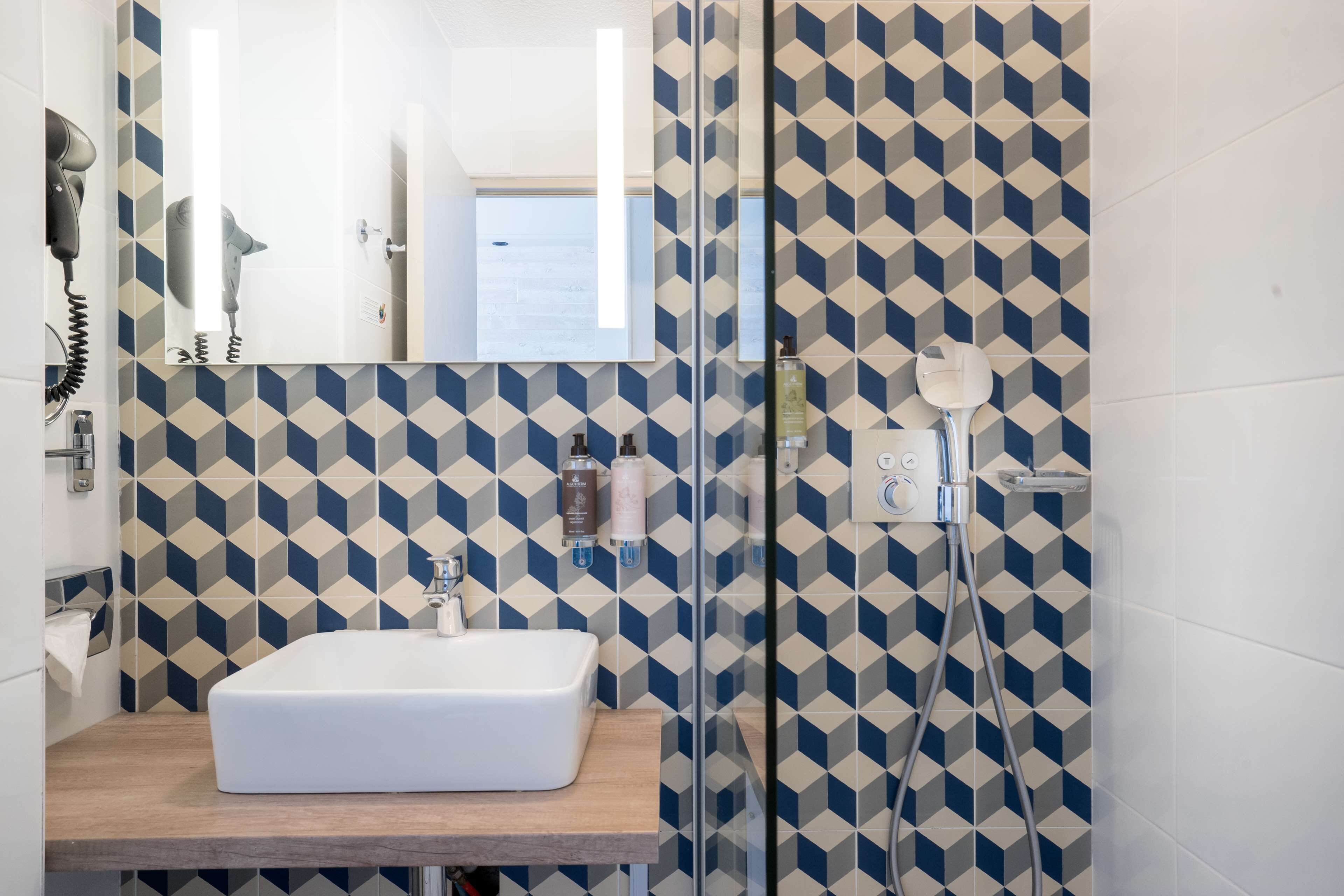 A bathroom with a geometric patterned wall, a white sink, and a glass shower enclosure.