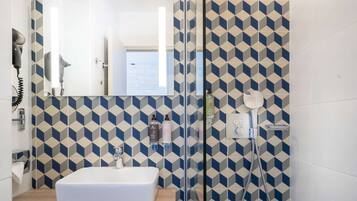 A bathroom with a geometric patterned wall, a white sink, and a glass shower enclosure.