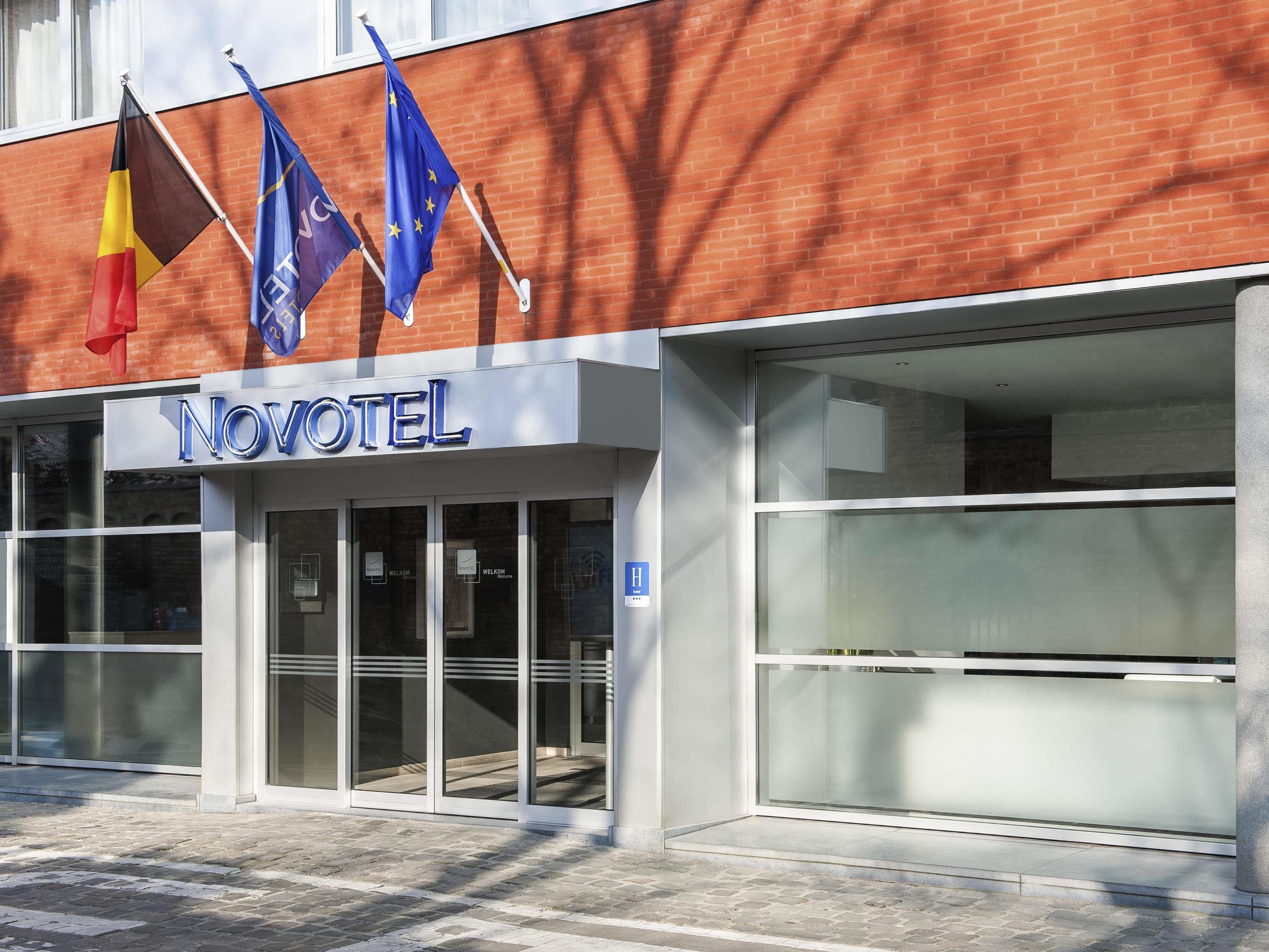 Un hotel con fachada moderna, grandes ventanales de vidrio y varias banderas, incluyendo la bandera de la UE.
