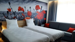 A hotel room with two beds, a grey sofa, and a large window with curtains.