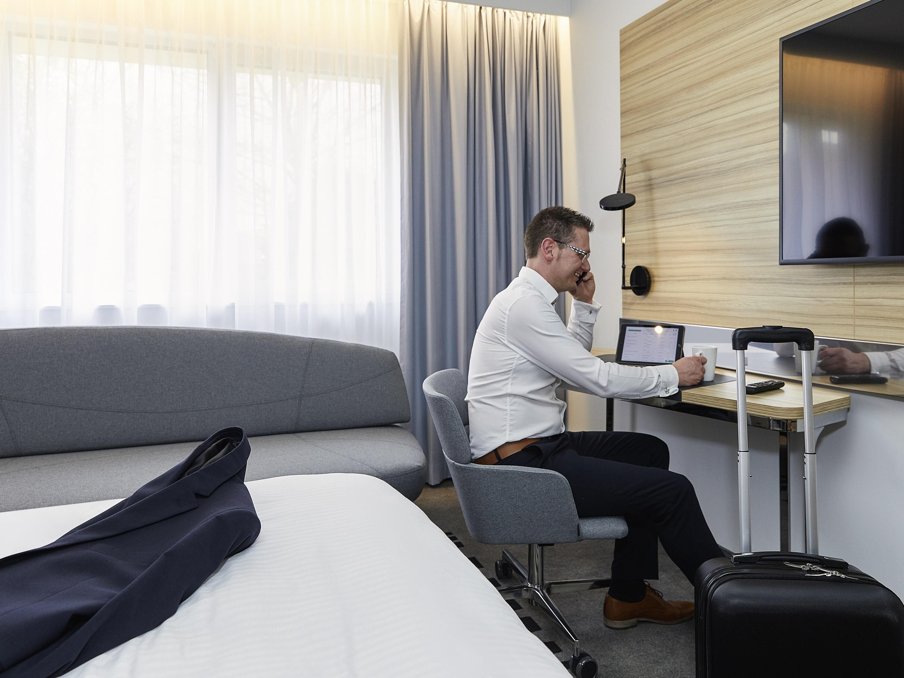 Een hotelkamer met een bed, een bureau met een laptop, een stoel en een koffer.