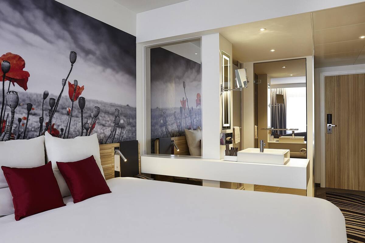 A modern hotel room with a large bed, a bedside table, a mirror, and a view of the bathroom.