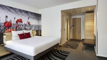 A modern hotel room with a large bed, a wall mural, and a wooden door.