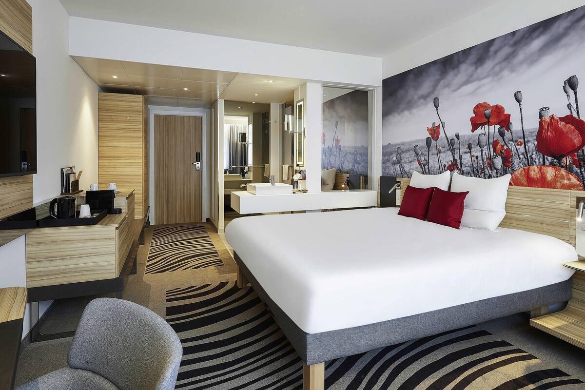 Een moderne hotelkamer met een groot bed, een bureau, een stoel, een badkamer met spiegel en een schilderij aan de muur.